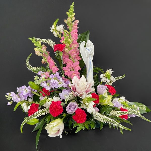 Sympathy floral arrangement with pink and white flowers and an angel figurine