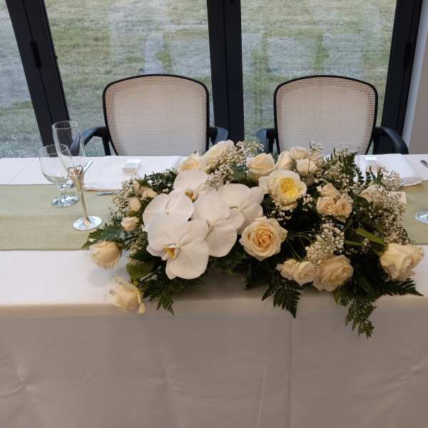 Low white floral centerpiece with roses and orchids on a table