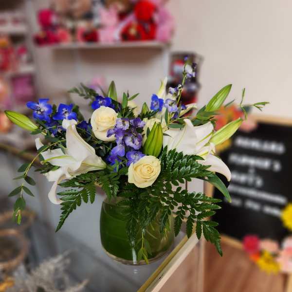 Bouquet of white lilies, cream roses, and blue flowers in a green glass vase