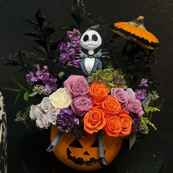 Halloween floral arrangement in a carved pumpkin with a skeleton figure and orange mushroom accent