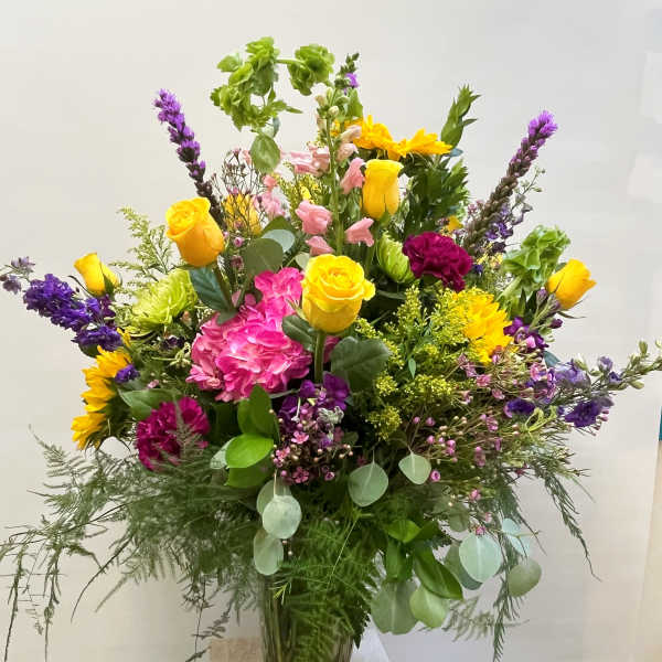 Mixed bouquet of yellow roses, pink hydrangea, and purple flowers in a glass vase