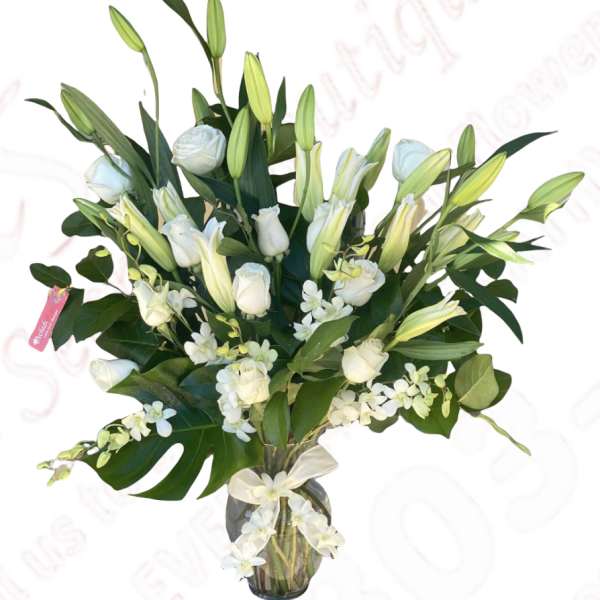 White roses and lilies in a glass vase with greenery