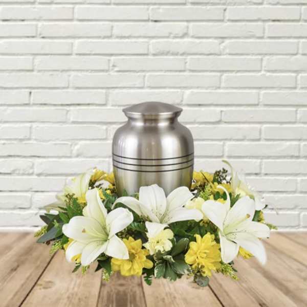 White lilies and yellow flowers arranged around a silver urn.