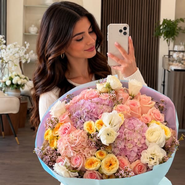 Woman holding a large pastel bouquet of roses, hydrangeas, and ranunculus