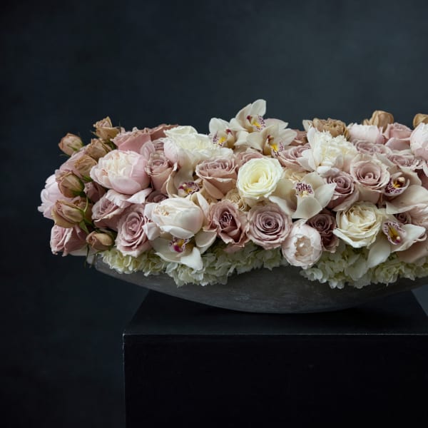 Low floral arrangement of blush and white roses with orchids in a dark bowl
