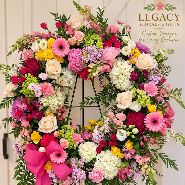 Heart-shaped floral wreath on a stand with pink, white, and yellow blooms