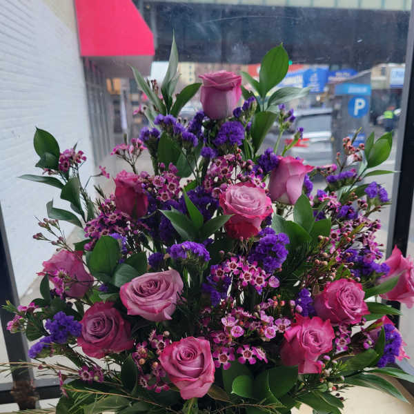 Basket arrangement of pink and purple roses with small filler flowers