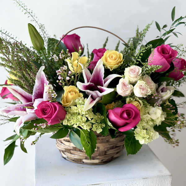 Basket arrangement of pink and yellow roses with white lilies