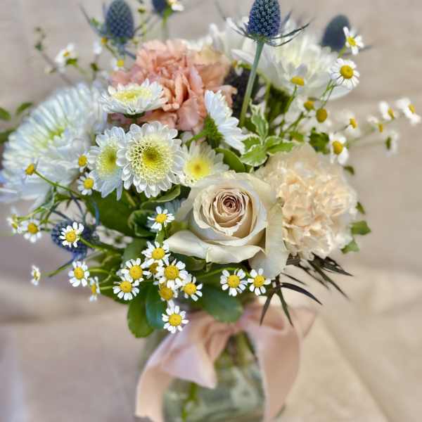Mixed bouquet with cream roses, peach carnations, and small white daisies in a glass vase