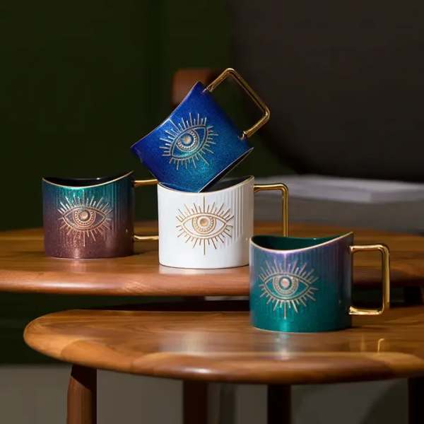 Four decorative mugs with gold handles and eye designs on a wooden table