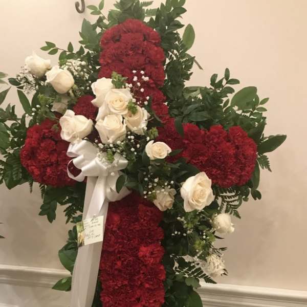 Red and white floral cross on an easel with a white ribbon