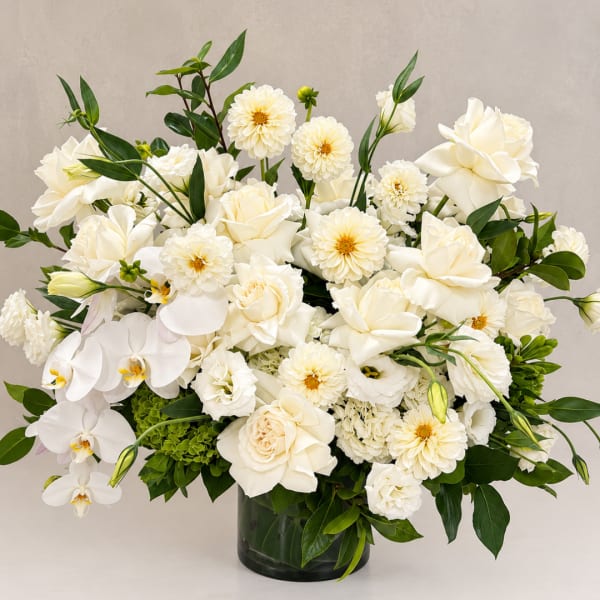 White floral arrangement in a dark glass vase with orchids and roses