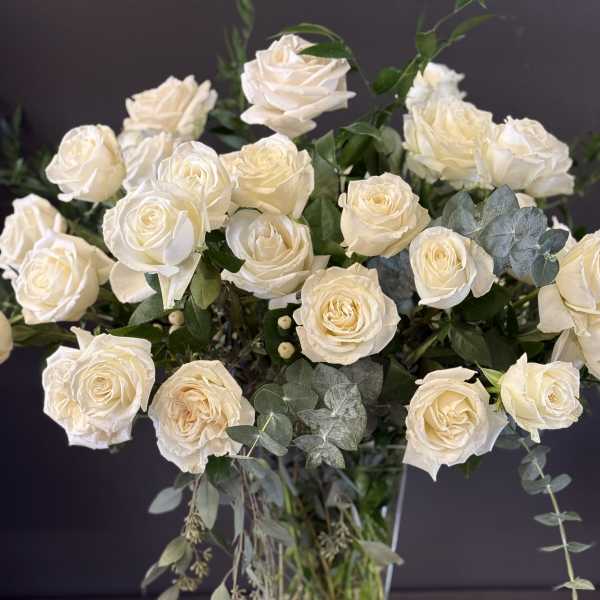 Cream roses arranged in a clear glass vase with eucalyptus