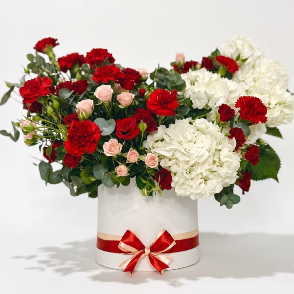 Red and white floral arrangement in a white hat box with a red ribbon