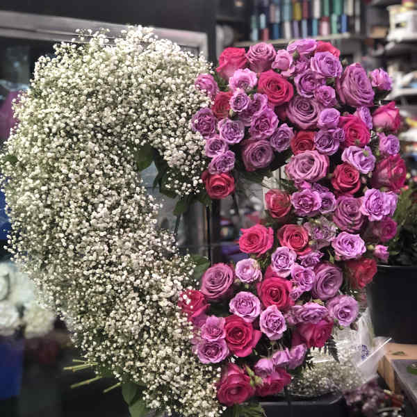 Heart-shaped floral arrangement of pink and purple roses with white baby's breath