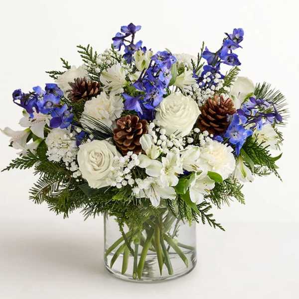 White and blue floral arrangement in a clear glass vase with pinecones