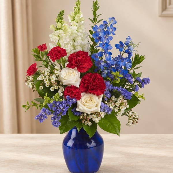 Mixed bouquet of red carnations, white roses, and blue flowers in a cobalt vase