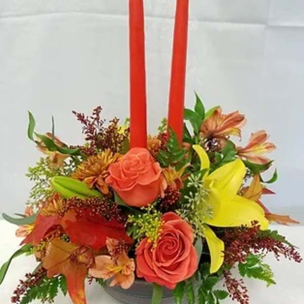 Floral centerpiece with two red taper candles and mixed orange, yellow, and pink blooms
