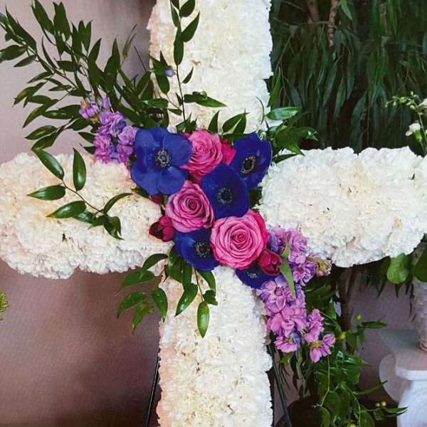 White floral cross on an easel with pink and blue flowers at the center