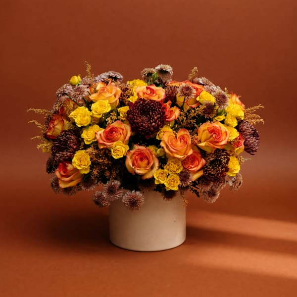 Mixed bouquet of orange roses and yellow spray roses in a white vase