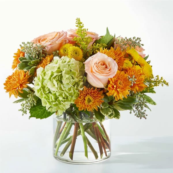 Peach roses and orange mums in a clear glass vase
