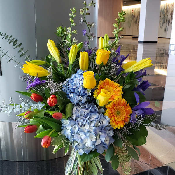 Colorful mixed bouquet in a clear glass vase with tulips, roses, hydrangeas, and gerbera daisies