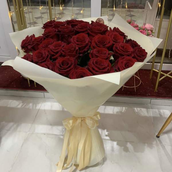 Large bouquet of red roses wrapped in white paper with a cream ribbon