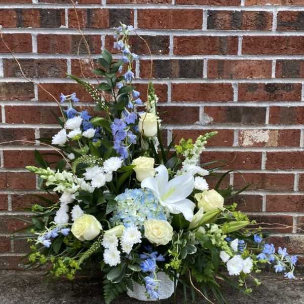 White and blue floral arrangement in a white basket against a brick wall