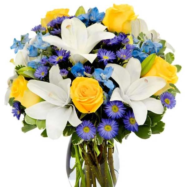 Bouquet of yellow roses, white lilies, and blue flowers in a glass vase