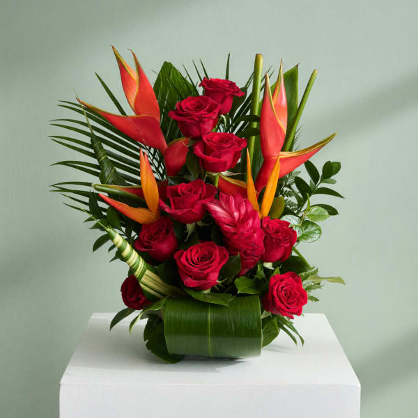 Red roses and tropical flowers arranged in a green vase