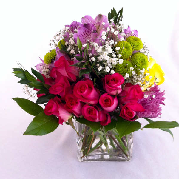 Mixed bouquet of pink roses, purple alstroemeria, and green pompons in a glass vase