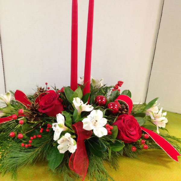 Red roses and white flowers in a low holiday centerpiece with tall red candles