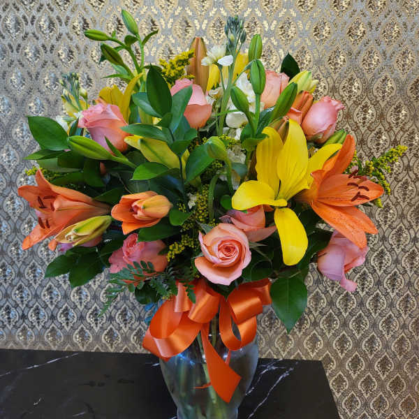 Bouquet of pink roses and lilies in a glass vase with an orange ribbon