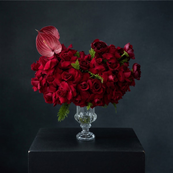 Red rose arrangement in a clear glass vase with a pink anthurium accent