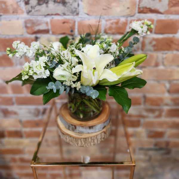 White lilies and small white flowers in a glass vase