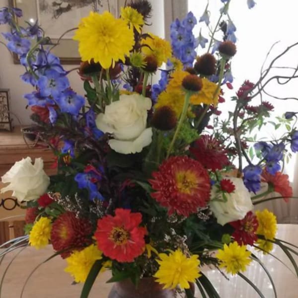 Tall mixed flower arrangement in a brown vase with blue, yellow, red, and white blooms