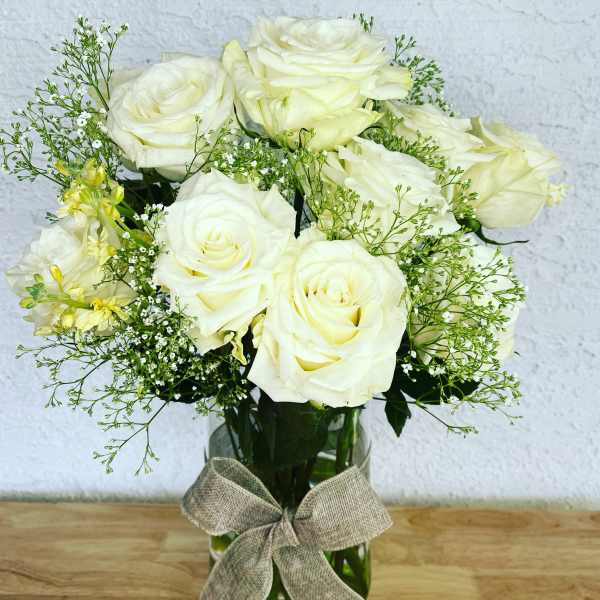 White roses arranged in a glass vase with a burlap bow