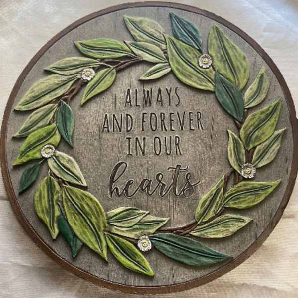 Round wooden wall sign with leafy wreath and the words "Always and Forever in Our Hearts"
