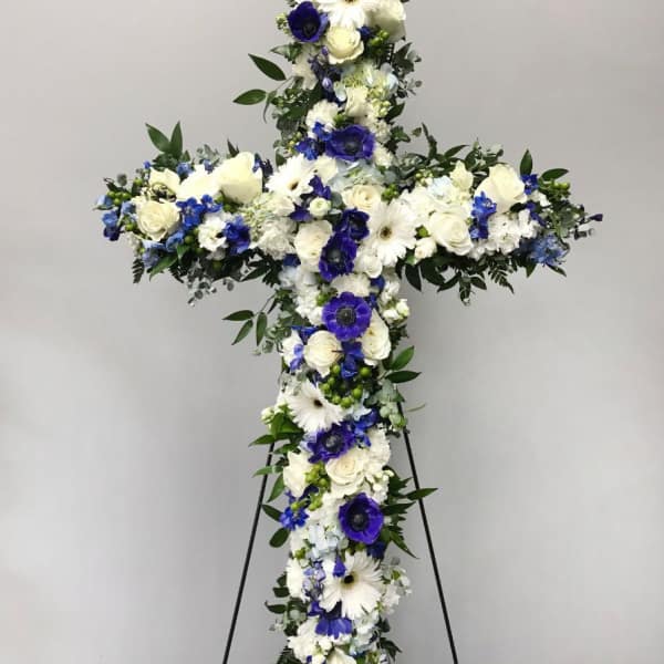 Standing floral cross of white and blue flowers on a metal easel