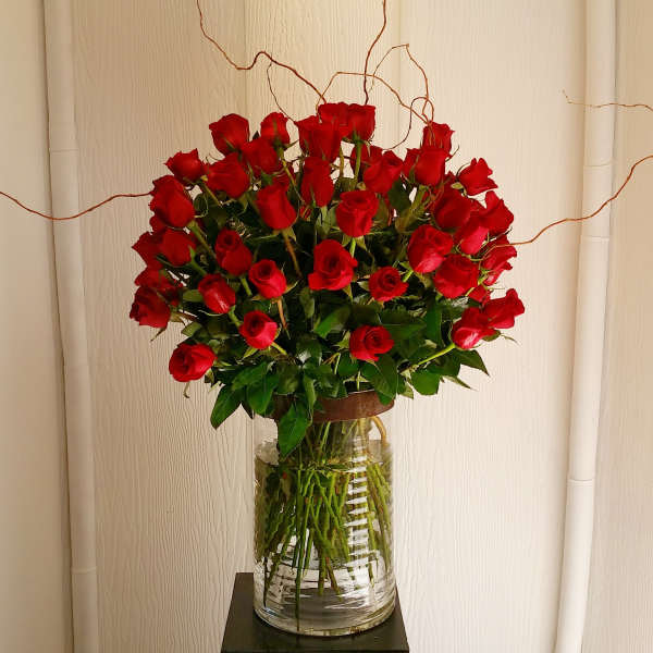 A tall bouquet of red roses in a clear glass vase