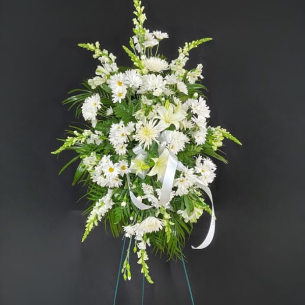 Tall standing spray of white flowers with a white ribbon on an easel stand