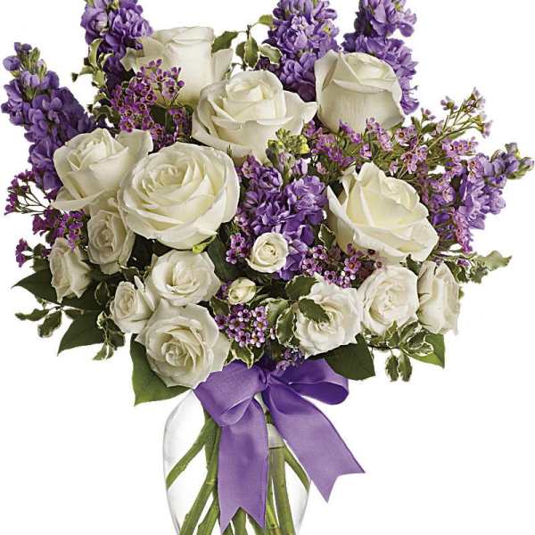 White roses and purple flowers in a glass vase with a purple ribbon