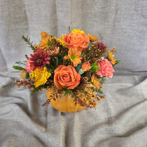 Orange roses and mixed fall flowers arranged in a pumpkin container