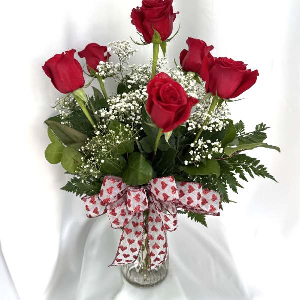Red roses in a clear glass vase with a heart-pattern ribbon