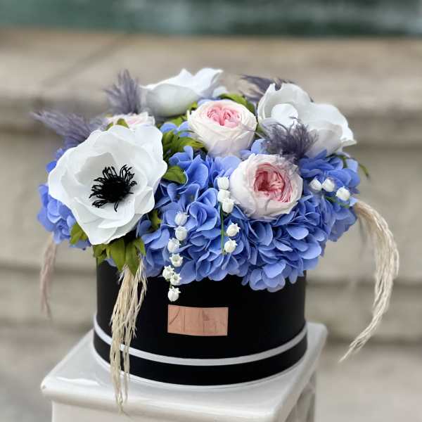 Blue hydrangeas with white and pink flowers in a black hatbox