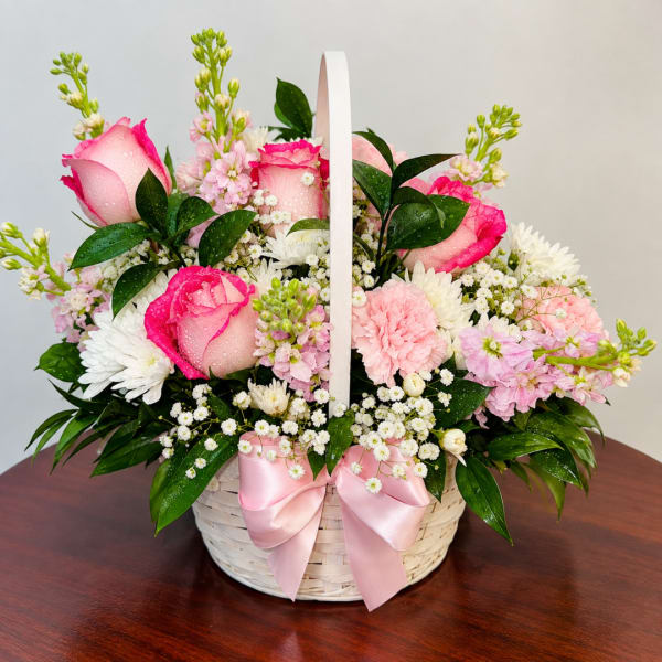 Pink roses and white daisies in a white basket with a pink ribbon