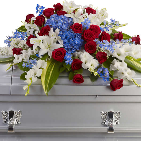 Red roses, white lilies, and blue flowers arranged on a silver casket