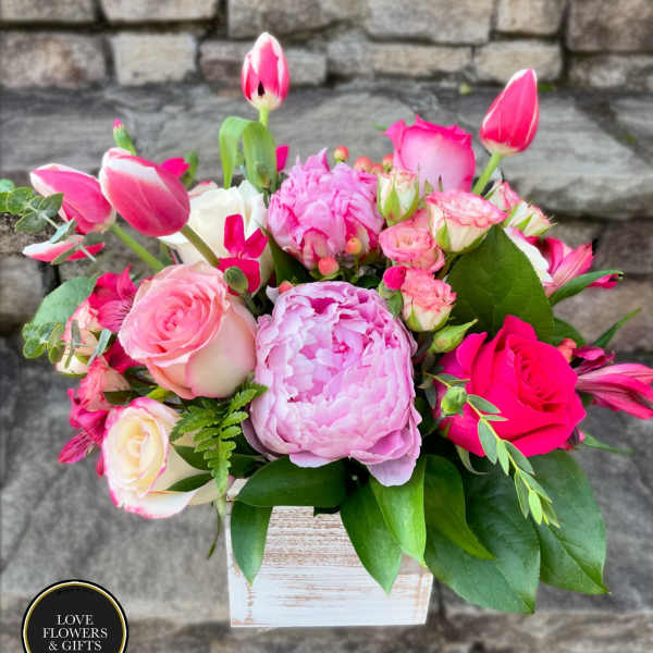 Pink and white peonies, roses, tulips, and other blooms in a whitewashed wood cube vase.