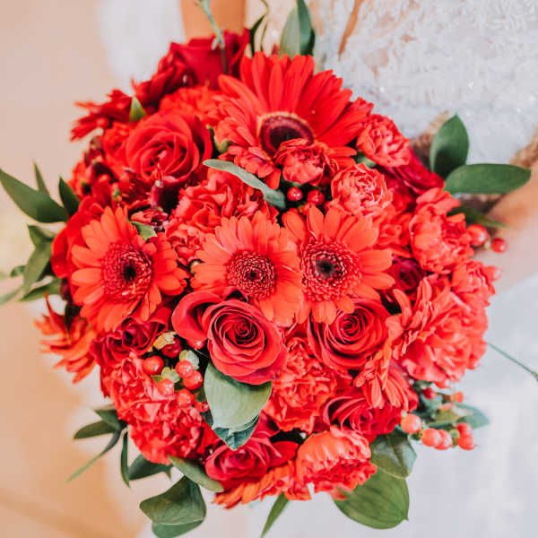 Bride holding a red bouquet with roses and gerbera daisies