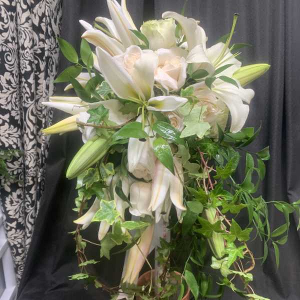 White lilies and pale roses in a copper vase with trailing ivy